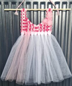 Handmade pink and white crochet top dress with a tutu skirt, hanging on a wooden rod against a corrugated metal background.