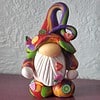 Colorful gnome figurine with a twisted hat, decorated with miniature fruit slices and a large white beard, set against a light background.