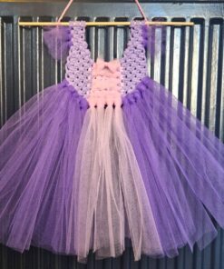 Lilac and pink tutu dress with a crocheted bodice, hanging on a crocheted loop against a corrugated metal background.