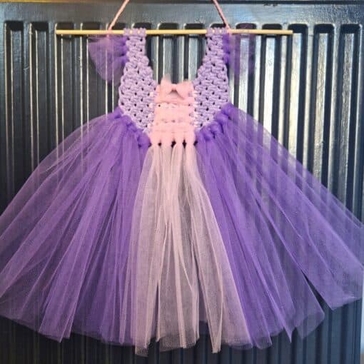 Lilac and pink tutu dress with a crocheted bodice, hanging on a crocheted loop against a corrugated metal background.