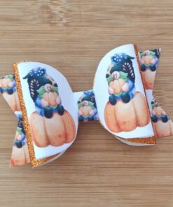 A decorative bow with a gnome sitting on a pumpkin design, featuring glittery orange edges, on a wooden surface.