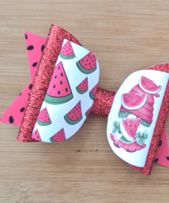 Red and white hair bow with glittery accents, featuring watermelon patterns and illustrations, set on a wooden background.