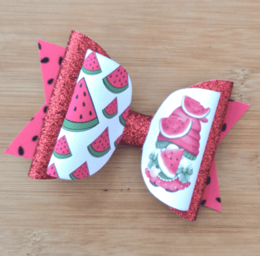 Red and white hair bow with glittery accents, featuring watermelon patterns and illustrations, set on a wooden background.