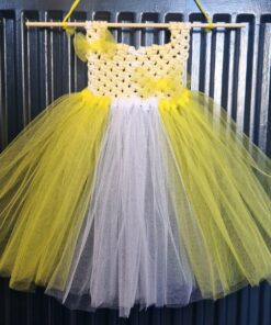 Yellow and white crocheted and tulle tutu dress hanging on a wooden dowel against a dark metallic background.