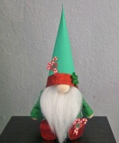 A festive gnome with a white beard, green hat, and red shoes decorated with candy canes, sitting on a black surface.