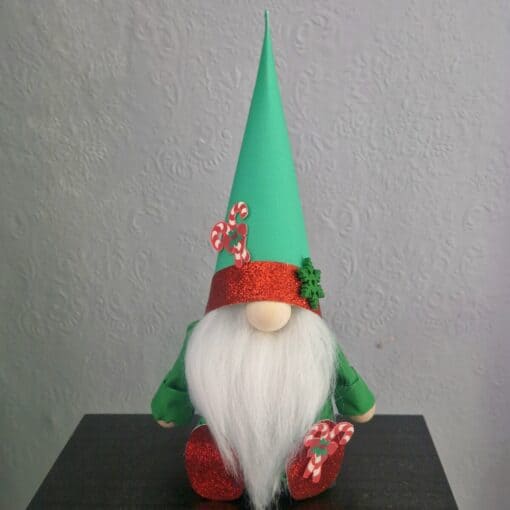 A festive gnome with a white beard, green hat, and red shoes decorated with candy canes, sitting on a black surface.