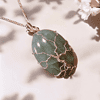 Silver tree of life pendant on green gemstone, surrounded by white cherry blossoms against a soft, shadowed background.