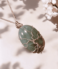 Silver tree of life pendant on green gemstone, surrounded by white cherry blossoms against a soft, shadowed background.