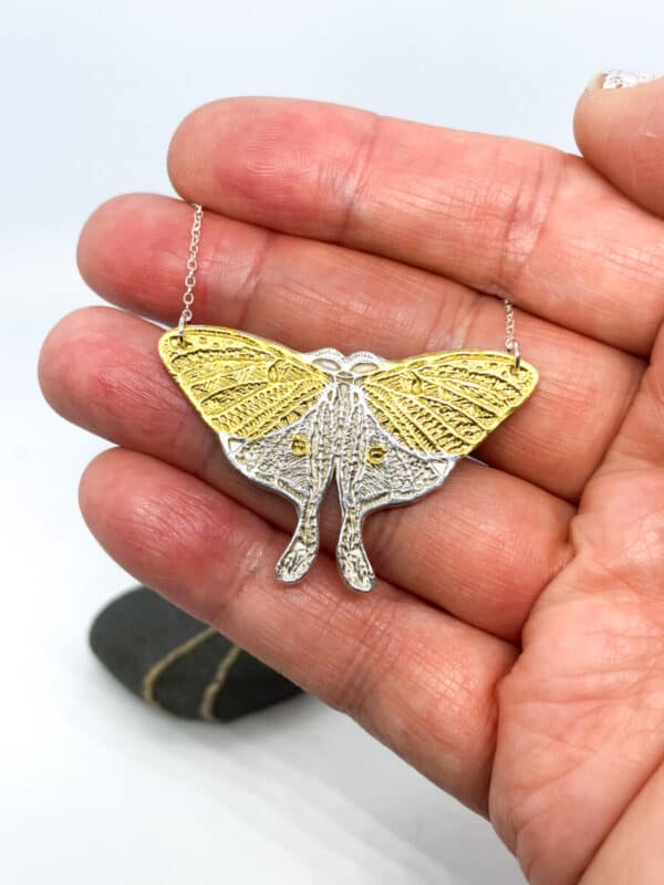 Hand holding a butterfly-shaped pendant with intricate gold and silver details.