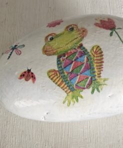 A painted white rock with a colorful frog design, flowers, a dragonfly, and a ladybug next to a green ruler.