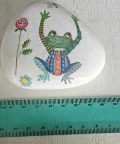 Painted stone with a colorful frog in a striped and polka-dotted outfit, next to a 15 cm green measuring ruler.