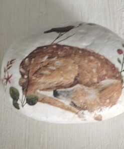 Painted stone featuring a curled-up fawn and foliage, next to a green ruler for scale measurement on a light wooden surface.