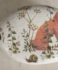 A painted rock with a fox, plants, and a snail, placed next to a green ruler for scale.