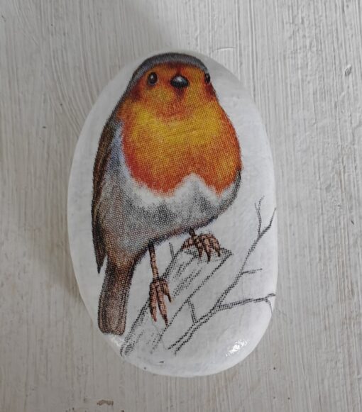 A painted rock with a detailed image of a robin perched on a branch, displayed on a light wooden surface.