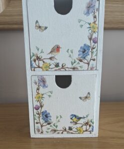 White wooden box with two drawers decorated with floral patterns, birds, and butterflies, placed on a wooden surface.