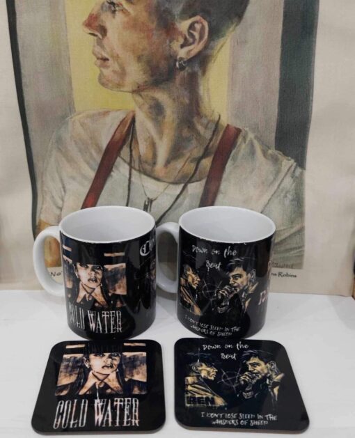 Two mugs and coasters with vintage-style art designs in front of a painting of a person looking to the left.