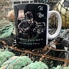 A black mug with an illustration of a guitarist, labeled "Hi Ren," resting on a fishing net outdoors.