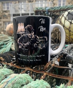 A black mug with an illustration of a guitarist, labeled "Hi Ren," resting on a fishing net outdoors.