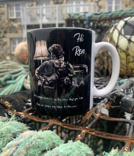 A black mug with an illustration of a guitarist, labeled "Hi Ren," resting on a fishing net outdoors.