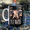 Mug on a net with an edgy black and white portrait and the text "Cold Water" outdoors near boats.