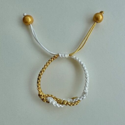 A braided bracelet with gold and white threads, adjustable knots, and gold bead accents on a light background.