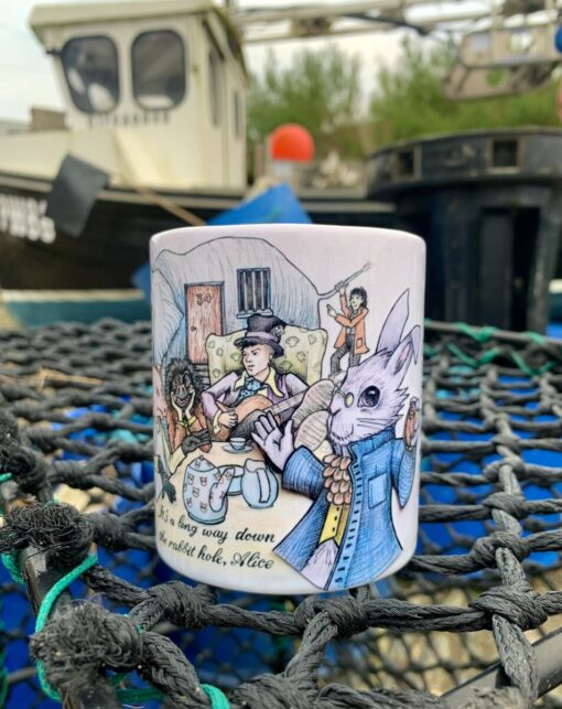 A mug with Alice in Wonderland characters, placed on fishing net, boat in background. Text: "It's a long way down the rabbit hole, Alice.