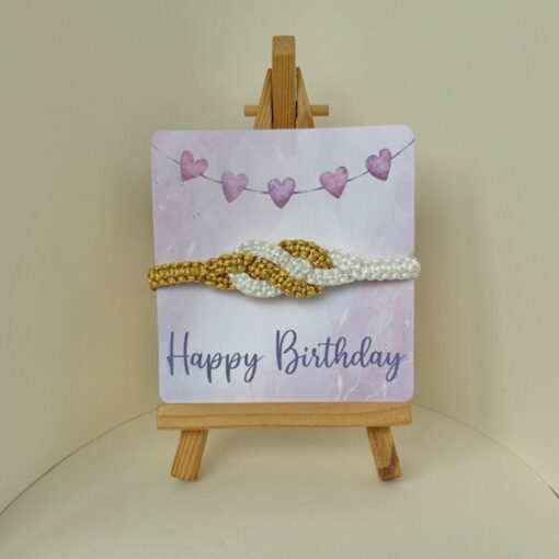 Birthday card with "Happy Birthday" text, featuring a knotted white and gold beaded headband on a small easel.