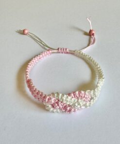 Handmade pink and white macrame bracelet with adjustable knot and beaded ends, displayed on a white background.