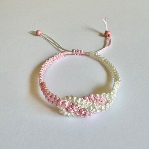 Handmade pink and white macrame bracelet with adjustable knot and beaded ends, displayed on a white background.