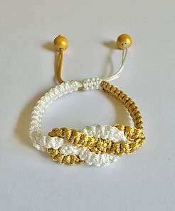 Handwoven bracelet made of white and gold thread with wooden beads, laid on a white surface.