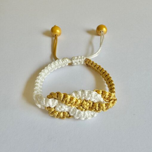 Handwoven bracelet made of white and gold thread with wooden beads, laid on a white surface.