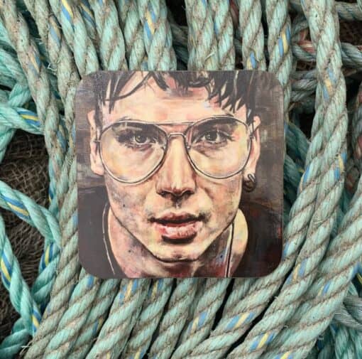 Artwork of a person with glasses on a square coaster, placed on intertwined ropes in blue and teal tones.