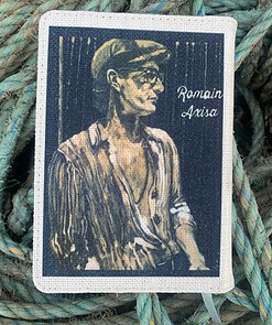 Vintage-style portrait of a man in a cap and glasses, overlaid on a textured fabric, with "Ronain Axisa" text.