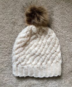 Hand knitted, cabled hat in cream Aran, with a removable synthetic pom pom in brown.