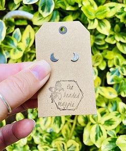 Hand holding tan tag with crescent moon earrings and 