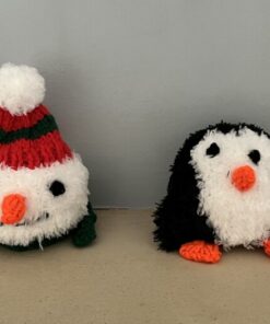 Four knitted plush toys: a reindeer, snowman, penguin, and Santa, lined up on a beige surface against a light blue wall.