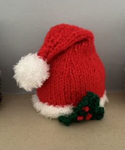 Knitted Christmas ornaments: two puddings and a Santa hat with holly decorations on a beige surface.