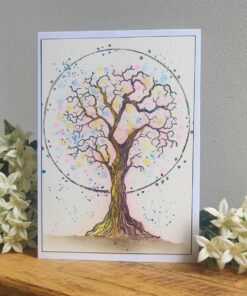 Watercolor painting of a tree with colorful leaves within a circle, surrounded by white flowers on a wooden surface.