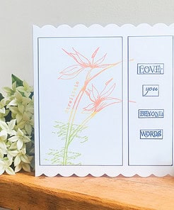 Greeting card on a wooden table featuring floral artwork and the words “Love you beyond words,” surrounded by white flowers.