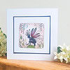 Greeting card featuring a fairy with red and blue wings, surrounded by flowers and foliage, placed on a wooden surface.