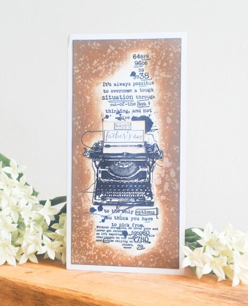 Father's Day card with a typewriter illustration, motivational text, and white flowers on a wooden surface.