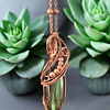 Copper-wrapped green stone pendant necklace displayed with two green succulent plants on a gray background.