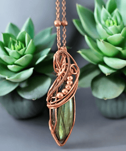 Copper-wrapped green stone pendant necklace displayed with two green succulent plants on a gray background.