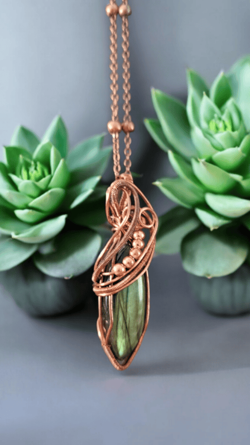 Copper-wrapped green stone pendant necklace displayed with two green succulent plants on a gray background.