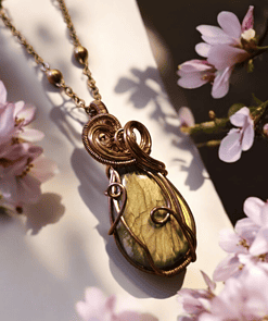 Wire-wrapped gemstone pendant necklace surrounded by pink flowers in soft focus.