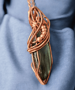 Copper wire-wrapped pendant with a dark stone centerpiece, displayed on blue fabric.