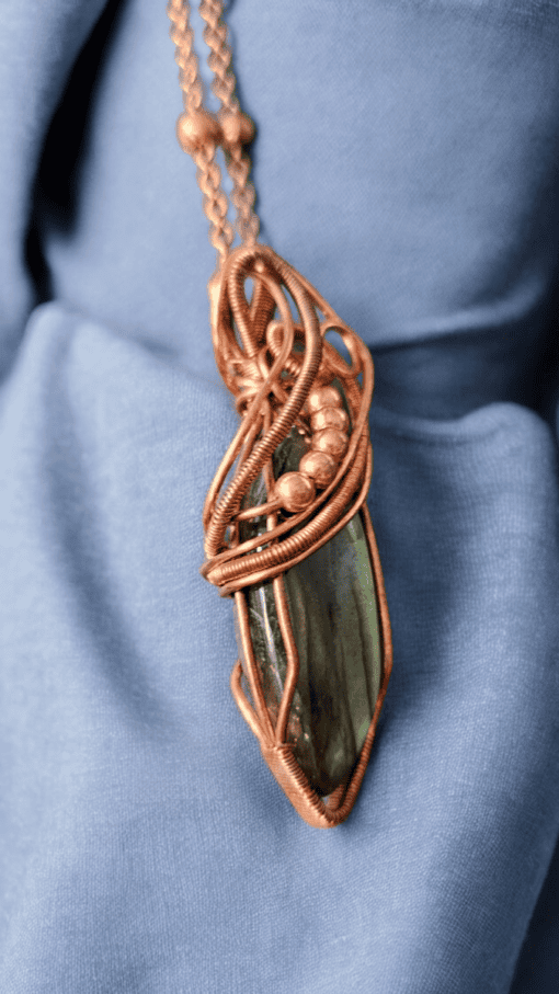 Copper wire-wrapped pendant with a dark stone centerpiece, displayed on blue fabric.