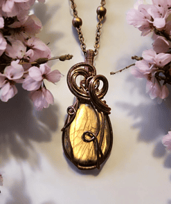 Gold wire-wrapped pendant on a bronze chain, surrounded by delicate pink cherry blossoms on a light background.