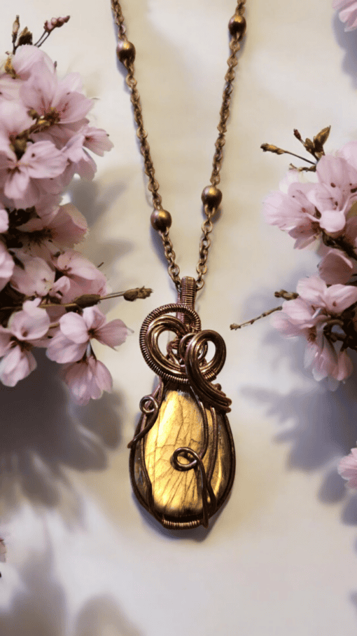 Gold wire-wrapped pendant on a bronze chain, surrounded by delicate pink cherry blossoms on a light background.