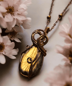 Gold and bronze pendant necklace with intricate wire wrapping, surrounded by soft-focused white flowers.